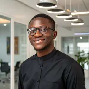 kwame-mensah Headshot of Kwame Mensah, a Ghanaian man with glasses and short hair, wearing a black shirt and smiling in an office hallway.